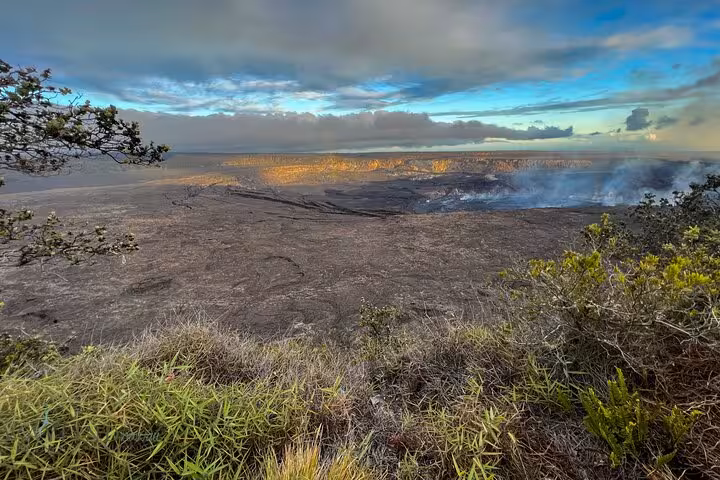 Breathtaking view of a volcanic landscape on the Big Island, featuring lush greenery and a smoking crater under a vibrant sky.