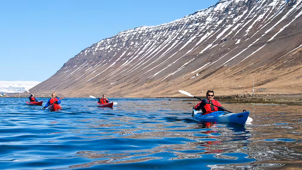 Group sea kayaking on clear blue water with dramatic mountain backdrop, a highlight of bike and kayak combo.