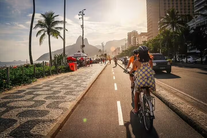 Biking along the vibrant Ipanema beach promenade, surrounded by palm trees and city views in Rio's golden sunlight.