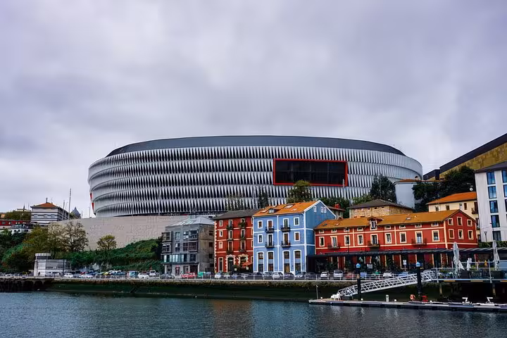View of Bilbao's modern stadium and colorful riverside buildings, showcasing a vibrant urban landscape.