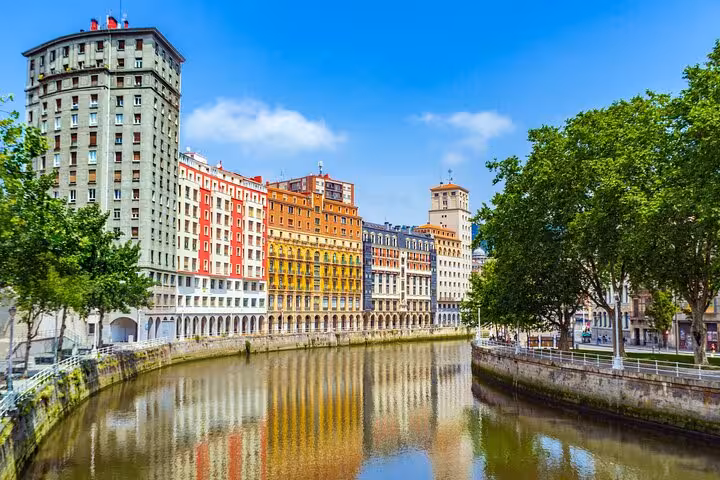 Scenic view of Bilbao's colorful riverside buildings along the Nervión River on a sunny day.