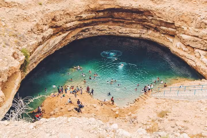 Tourists swimming in Bimmah Sinkhole stunning turquoise pool surrounded by limestone rocks in Oman Muscat tour