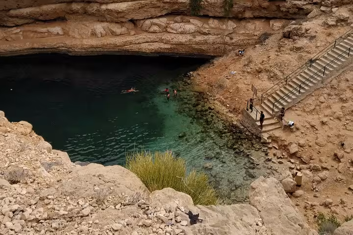 Aerial view of Bimmah Sinkhole turquoise waters with swimmers and stone staircase in Oman near Muscat