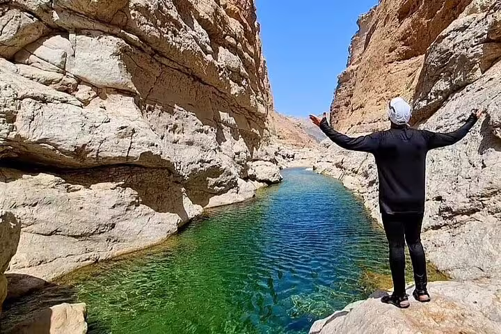 Traveler enjoys scenic views of turquoise waters and rugged rock formations at Wadi Al Arbeieen during full-day tour.