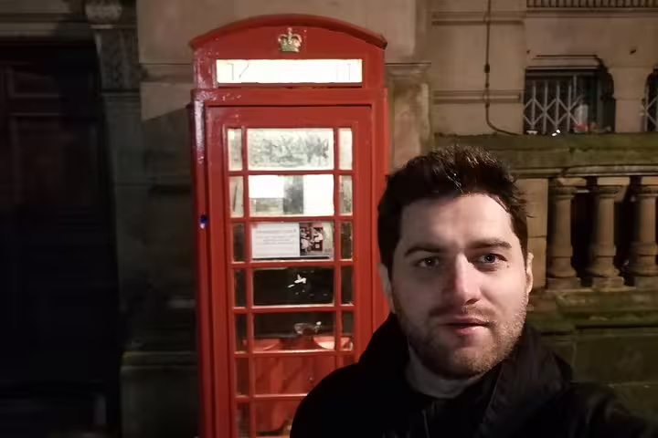 Man standing beside iconic red British telephone box at night in Birmingham