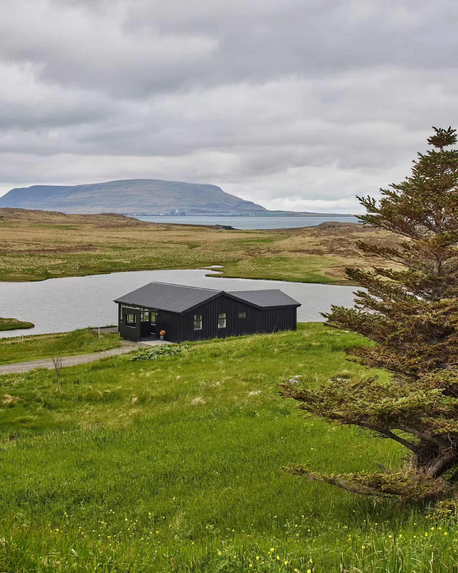 Secluded black cabin retreat nestled beside a tranquil lake with stunning Icelandic fjord and mountain backdrop