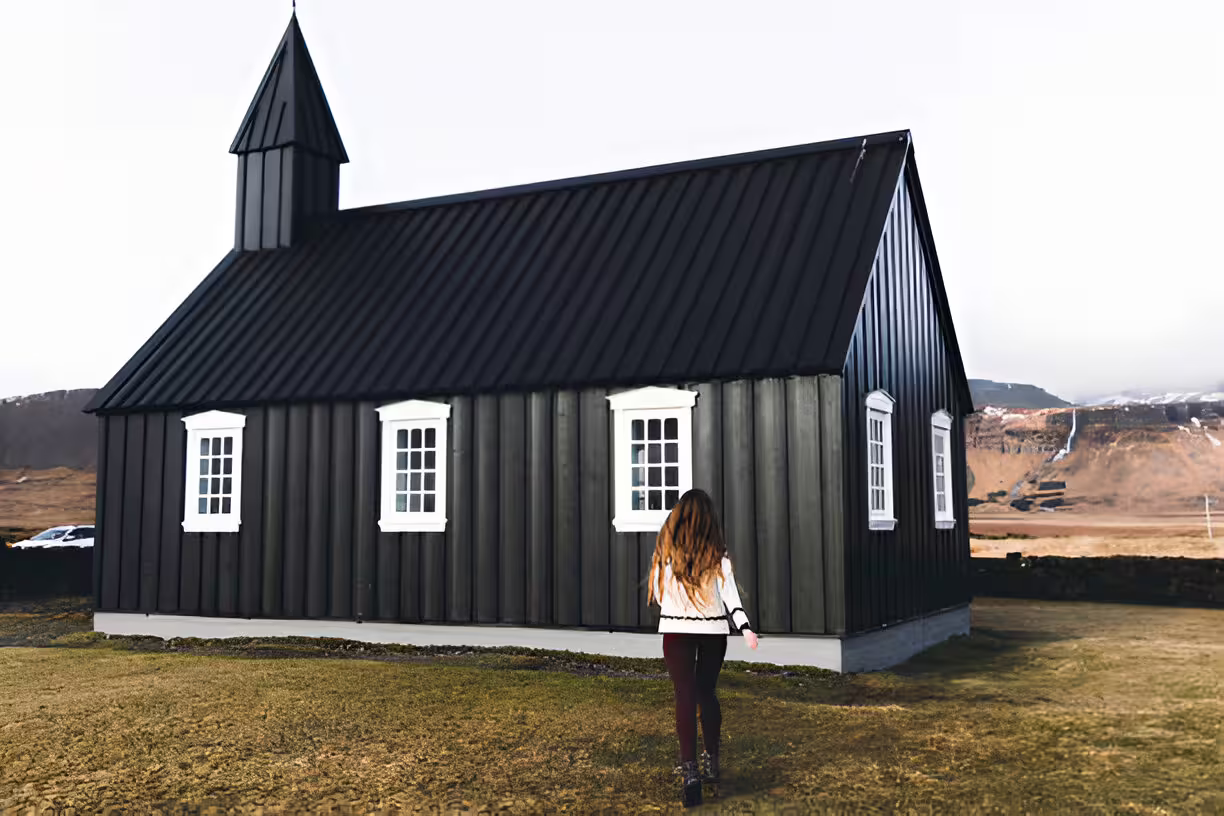 Woman walking toward iconic black Búðakirkja church on Snæfellsnes Peninsula, Iceland