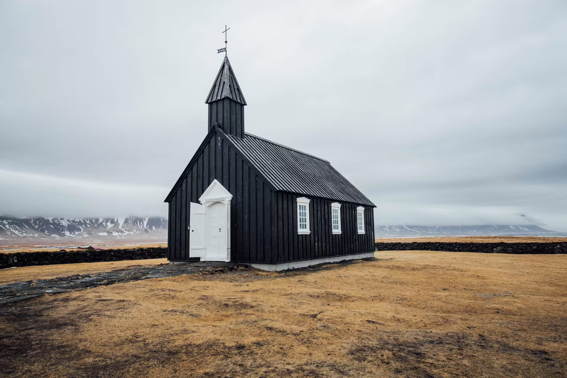 Black wooden church with white door and steeple on Iceland's Ring Road under overcast skies