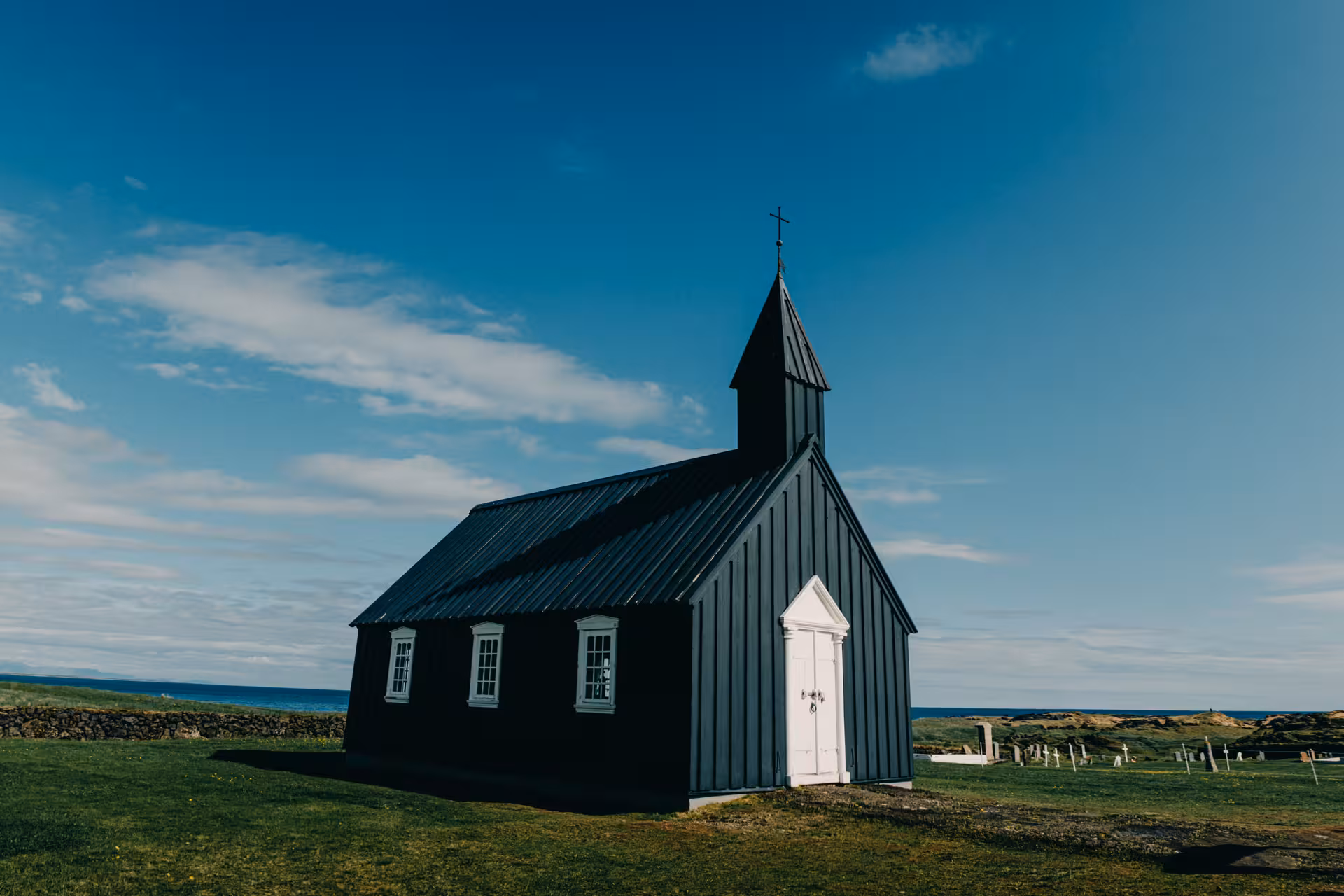 Black wooden church with white door and cross on green coastal landscape, Snaefellsnes Peninsula, Iceland