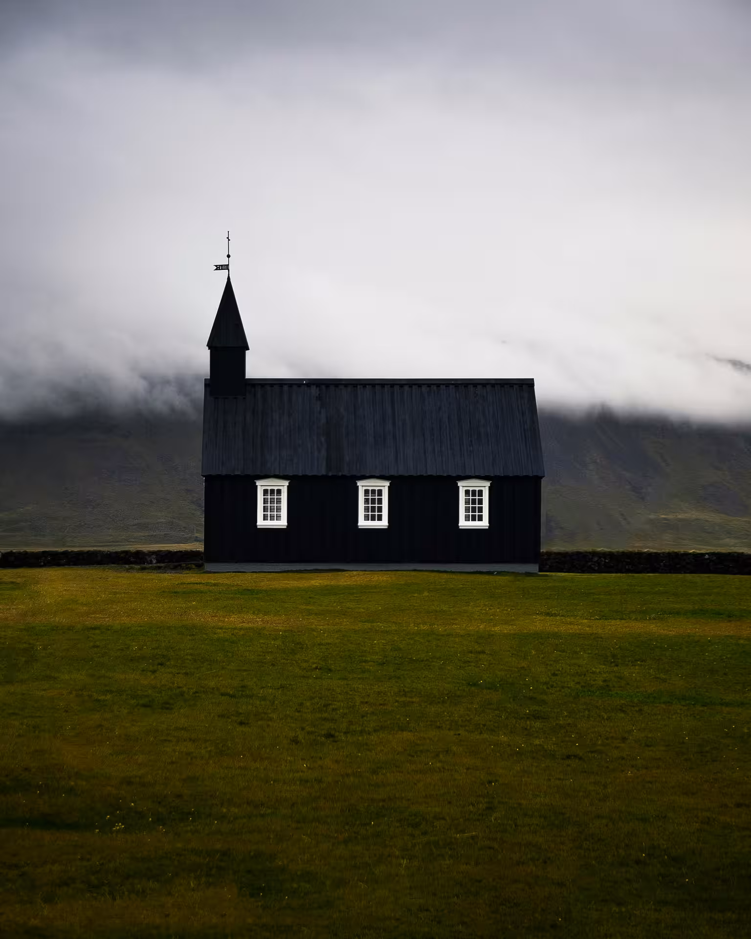 Black Búðakirkja church on Snæfellsnes Peninsula with dramatic misty mountains and green fields