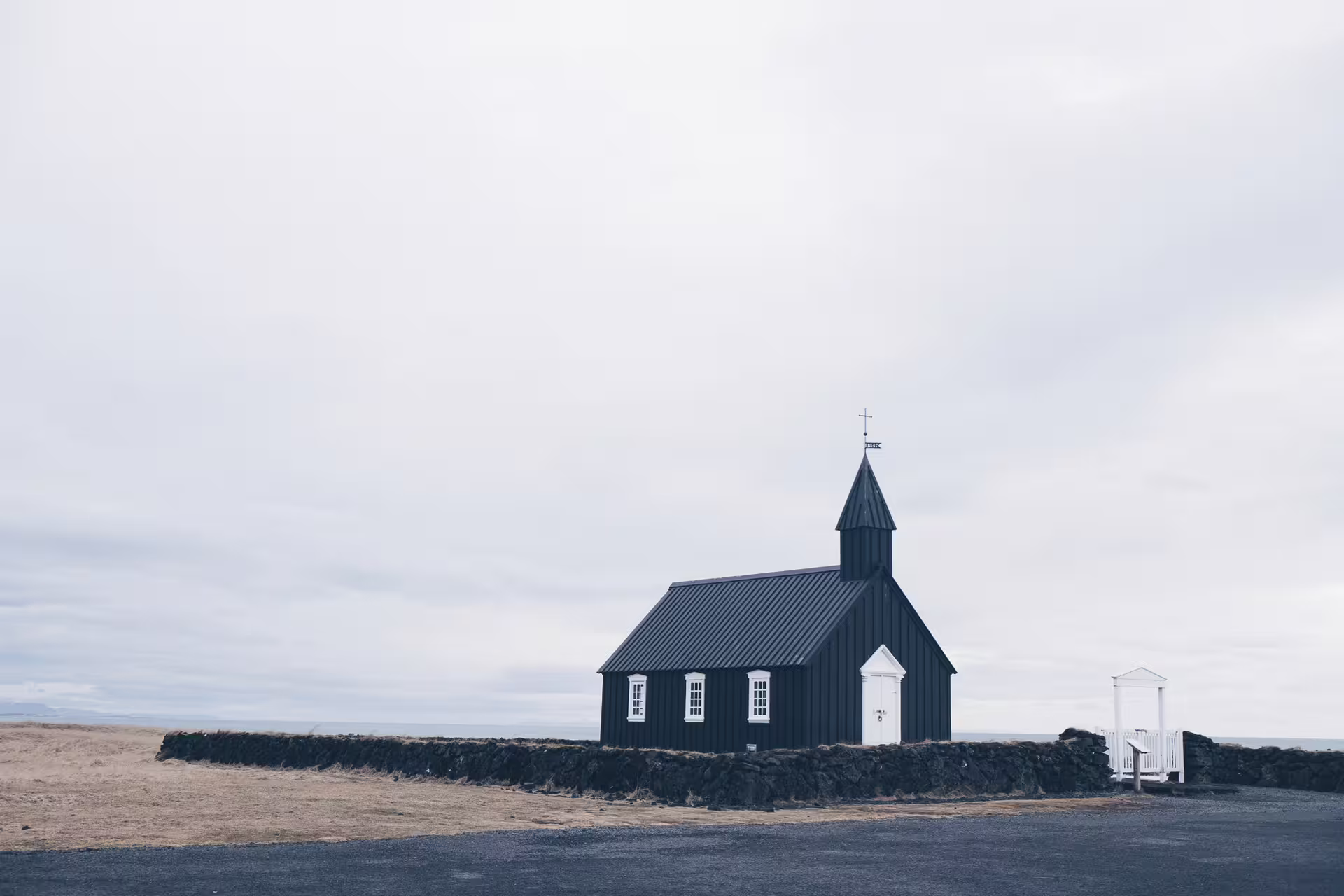 Black wooden church with white trim and steeple on Snaefellsnes Peninsula, Iceland, under overcast skies