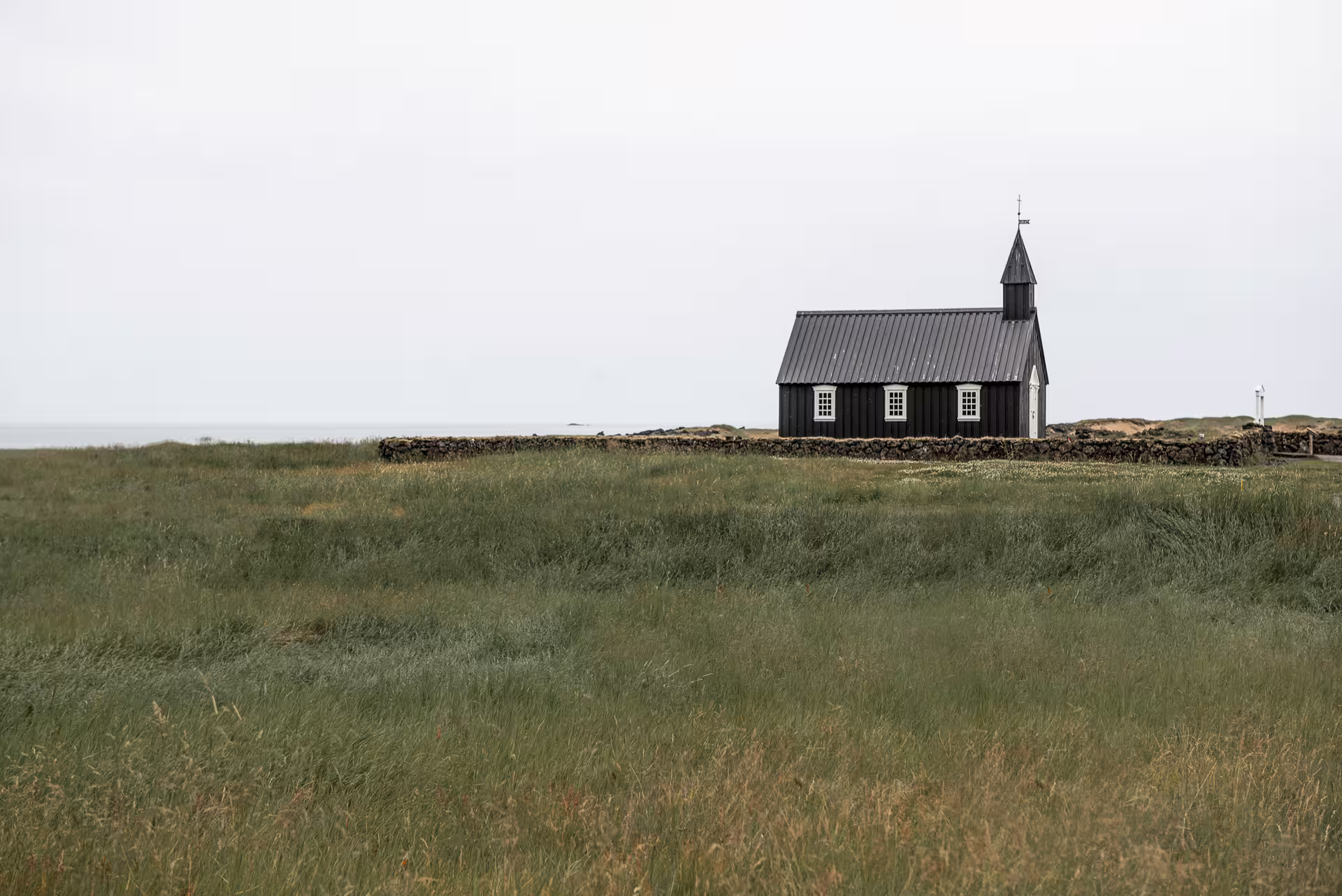 Black wooden church on Snaefellsnes Peninsula surrounded by green meadows and stone wall near the sea