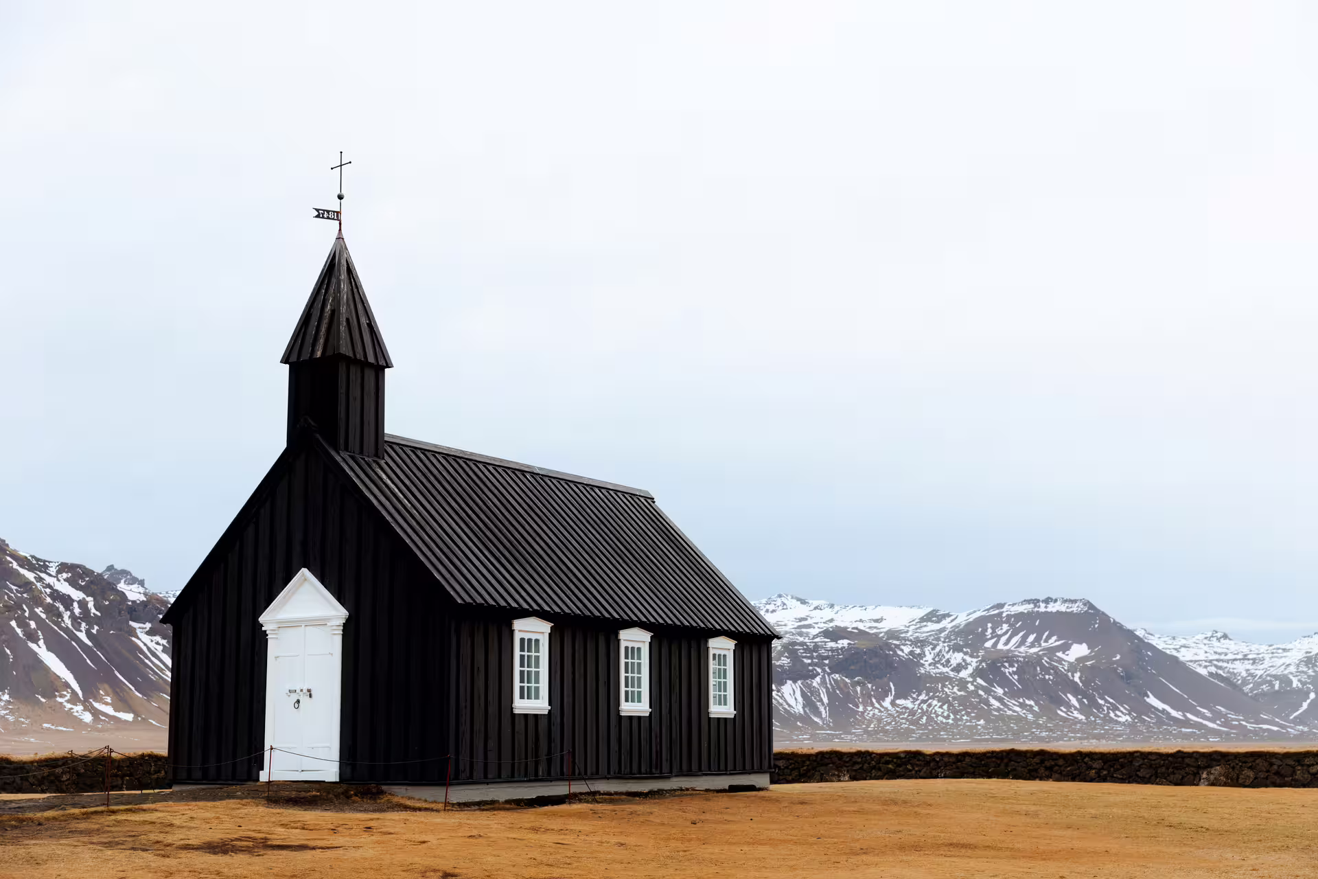 Black church with white trim and steeple on Snaefellsnes Peninsula, Iceland, with snow-capped mountains behind