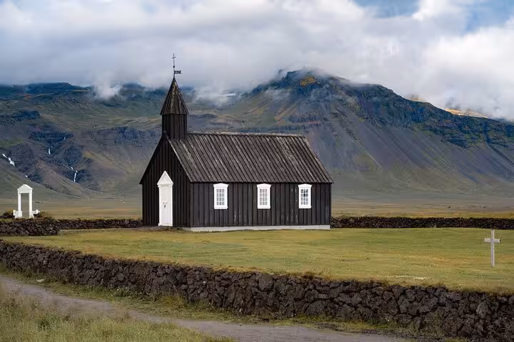 Black wooden church with white trim against dramatic mountains on Snaefellsnes Peninsula, Iceland