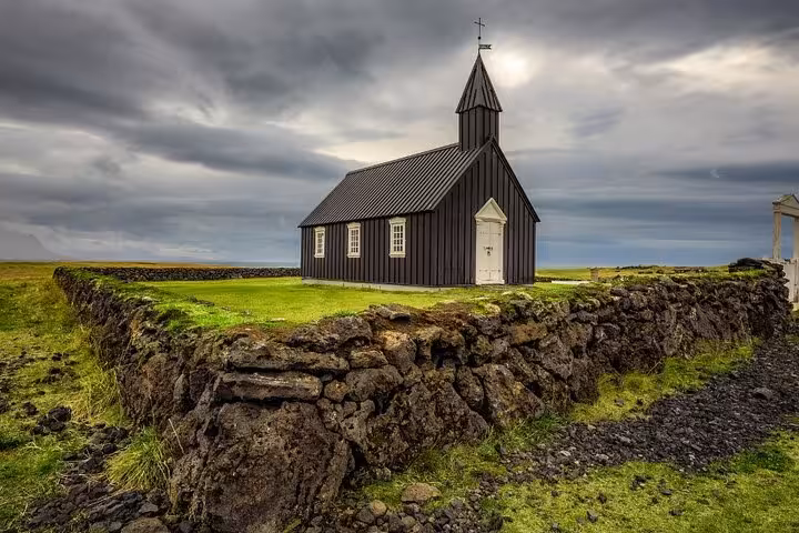 Black wooden church with steeple on green Snaefellsnes Peninsula, Iceland, under dramatic cloudy sky