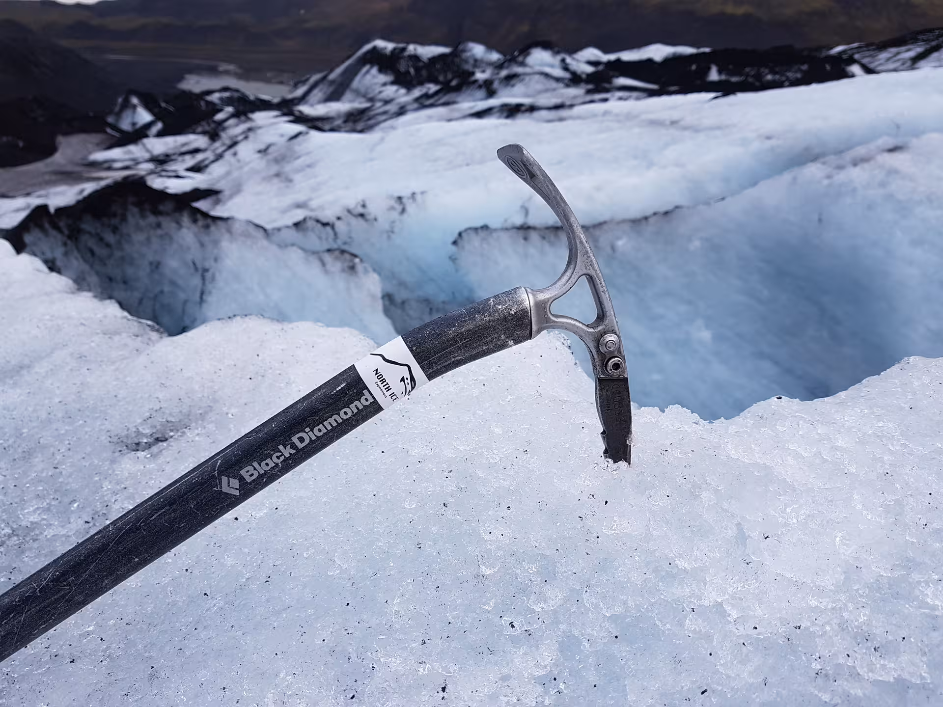 Black Diamond ice axe planted in glacier ice with crevasse and mountains in Iceland background