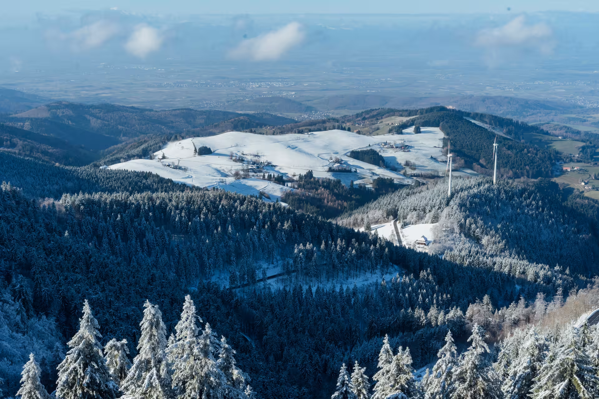 Aerial winter view of Black Forest snowy hills, evergreen trees, and wind turbine near Baden-Baden