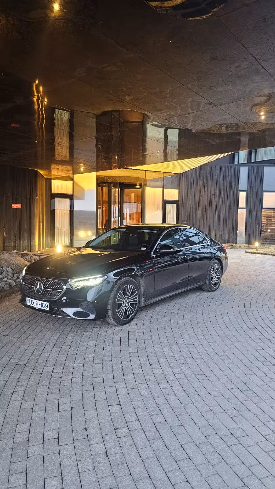 Black Mercedes-Benz luxury sedan parked at illuminated hotel entrance on cobblestone driveway in Iceland