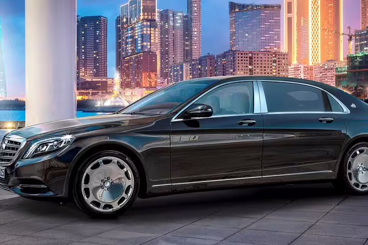 Black Mercedes-Maybach luxury sedan parked with illuminated city skyline at dusk