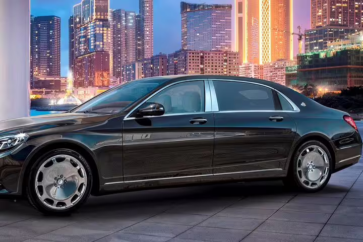 Black Mercedes-Maybach luxury sedan parked in front of illuminated city skyline at dusk