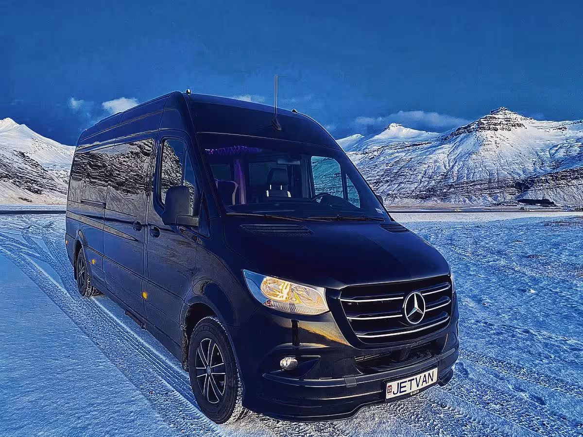 Black Mercedes Sprinter van parked on snowy Iceland road with snow-capped mountains in background