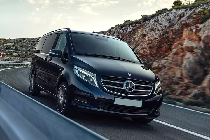 Black Mercedes-Benz V-Class minivan driving on a scenic road for private Paris tour