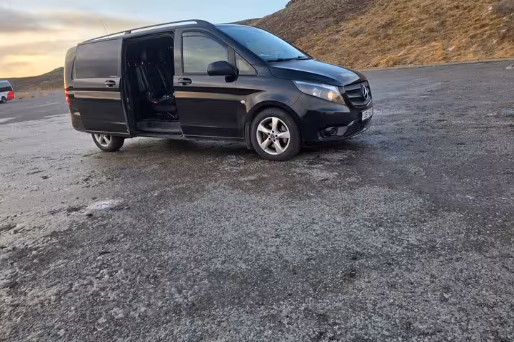 Black Mercedes-Benz minivan with open sliding door parked on gravel near hillside at sunset in Iceland