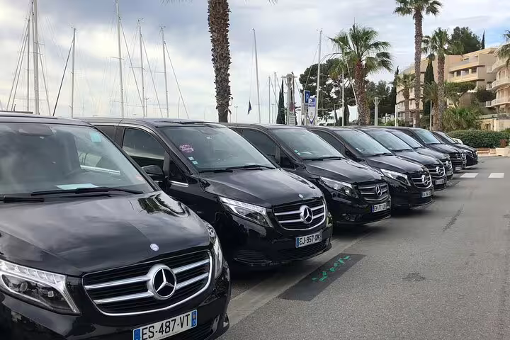Fleet of black Mercedes-Benz V-Class vans parked near a marina in southern France