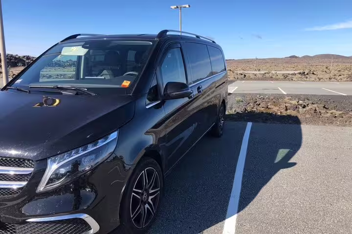 Black Mercedes-Benz V-Class minivan parked in Keflavik Airport parking lot with volcanic landscape
