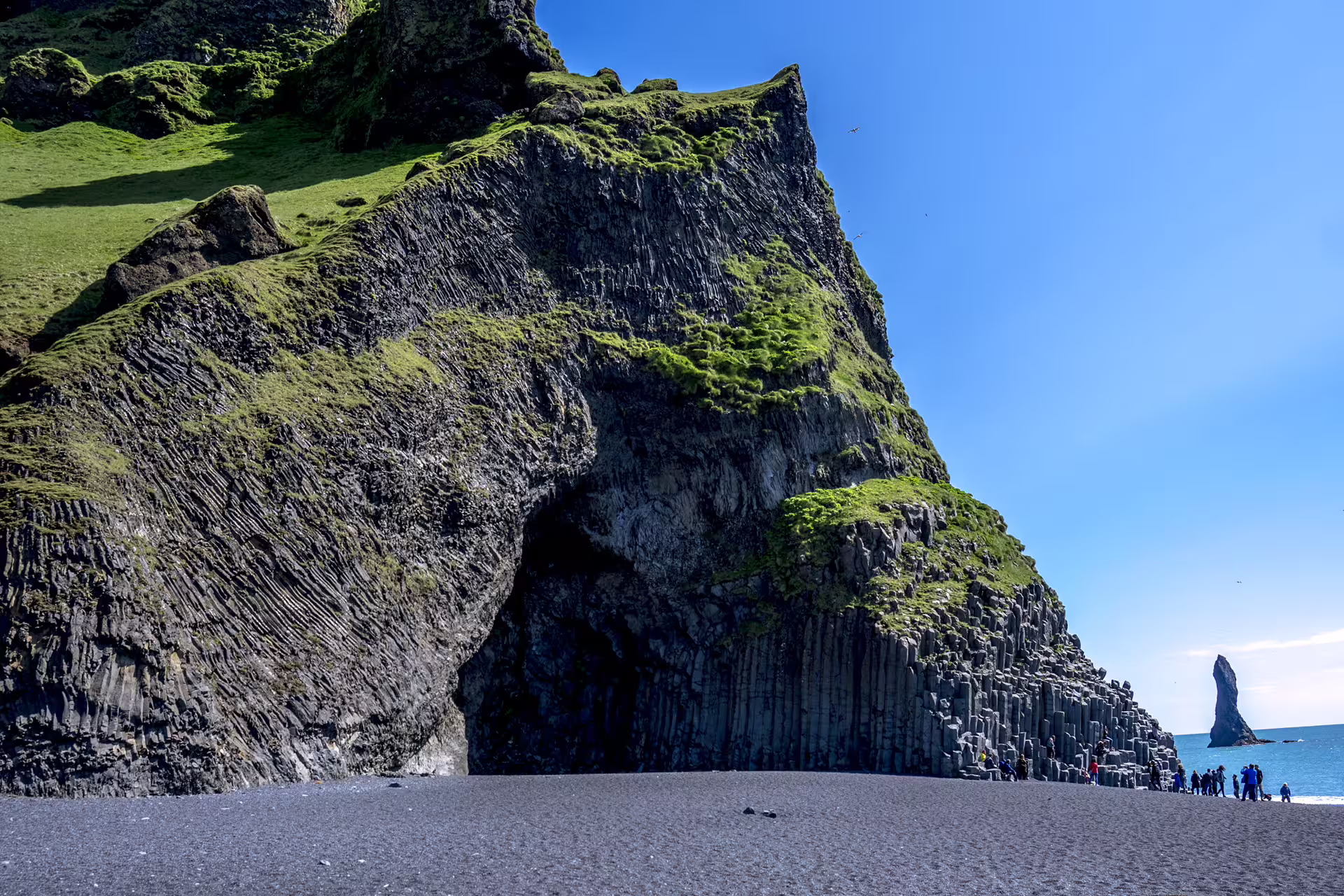 Black sand beach with towering basalt column cliffs and sea stack at Reynisfjara, Iceland
