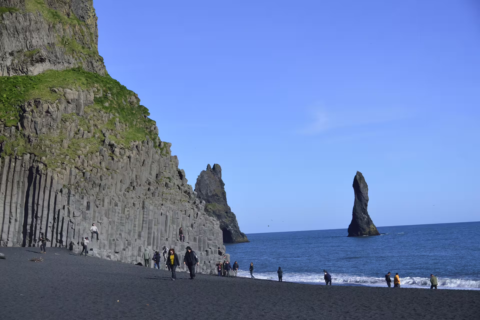 Tourists walking on Reynisfjara black sand beach with basalt columns and sea stacks in South Iceland