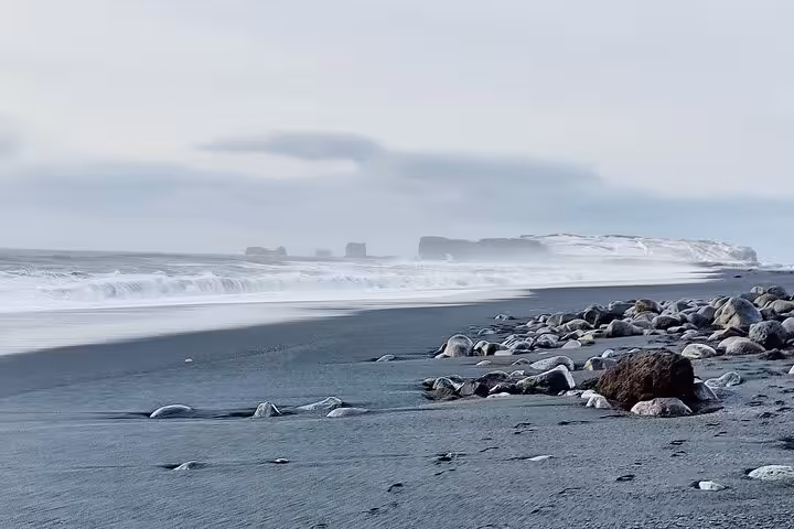 Black sand beach with scattered rocks and crashing waves on Iceland's South Coast