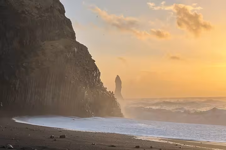 Black sand beach with dramatic sea stack and crashing waves at golden sunset, South Coast Iceland