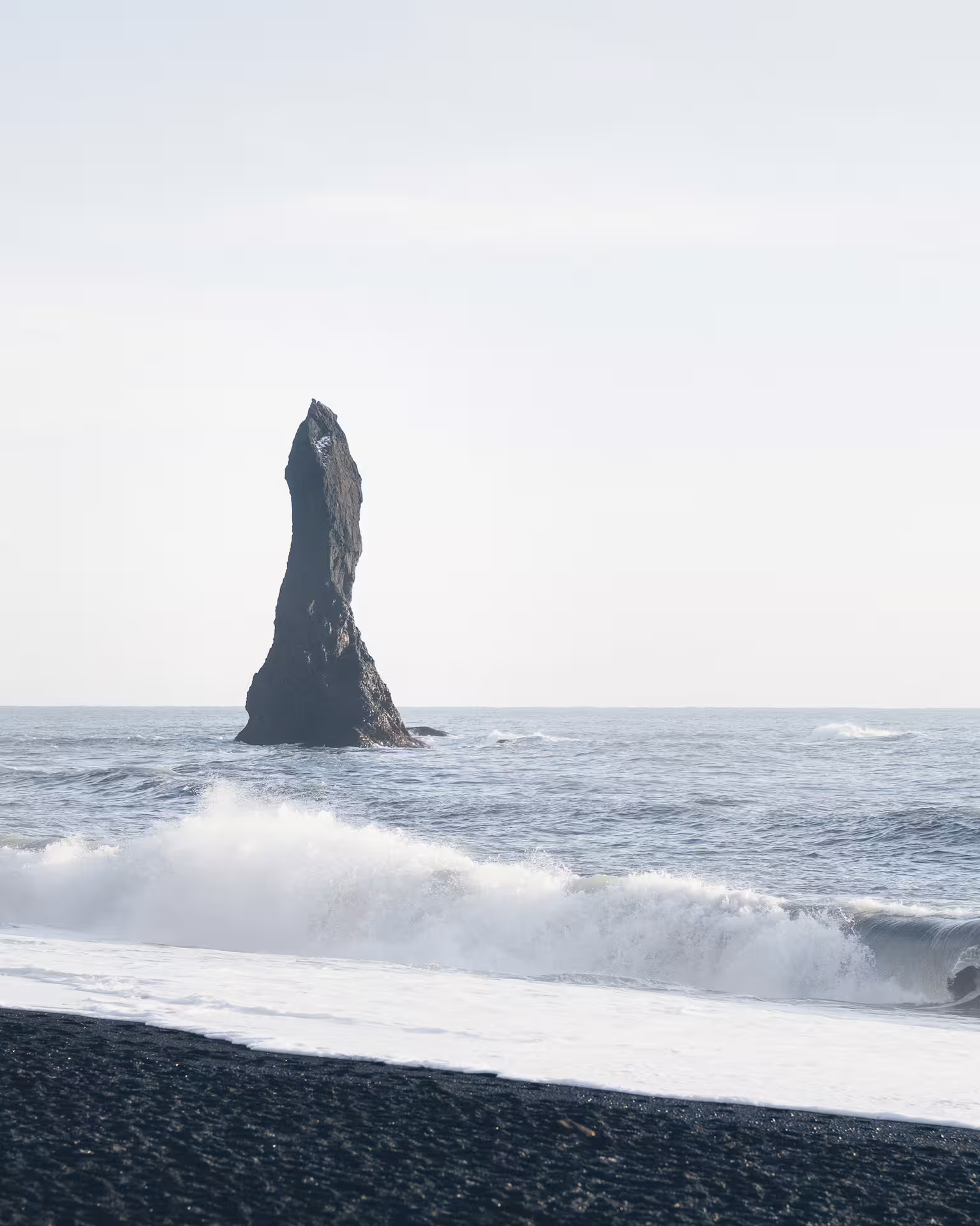 Tall black basalt sea stack rising from ocean waves on Iceland's black sand beach at Vik