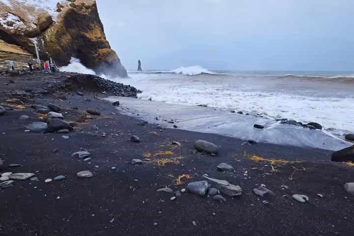 Black sand beach with volcanic rocks and crashing waves on Iceland's south coast under cloudy skies
