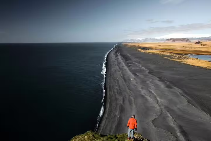 Person in red jacket overlooking Iceland's black sand beach coastline stretching toward distant mountains