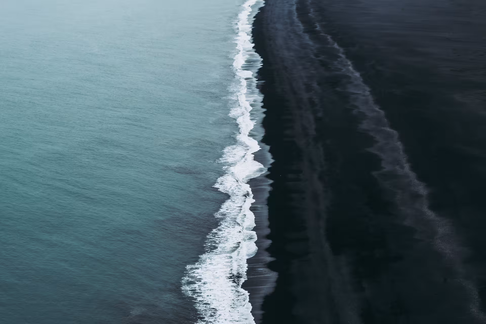 Aerial view of white waves washing onto Iceland's black sand beach along the South Coast