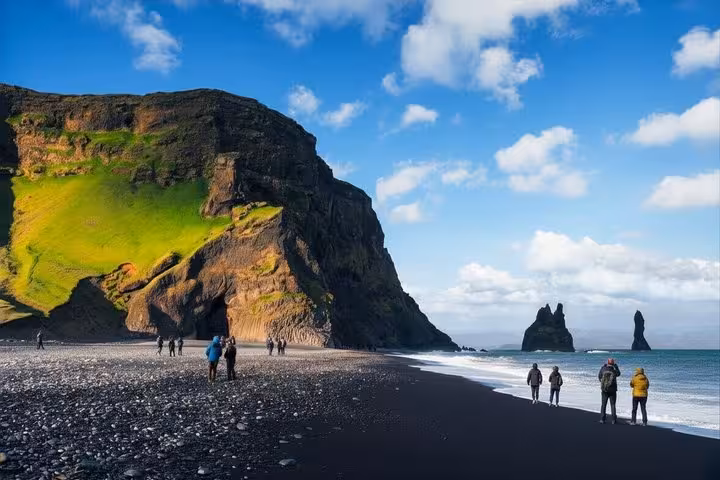 Tourists walking on Reynisfjara black sand beach with dramatic cliffs and sea stacks, South Coast Iceland