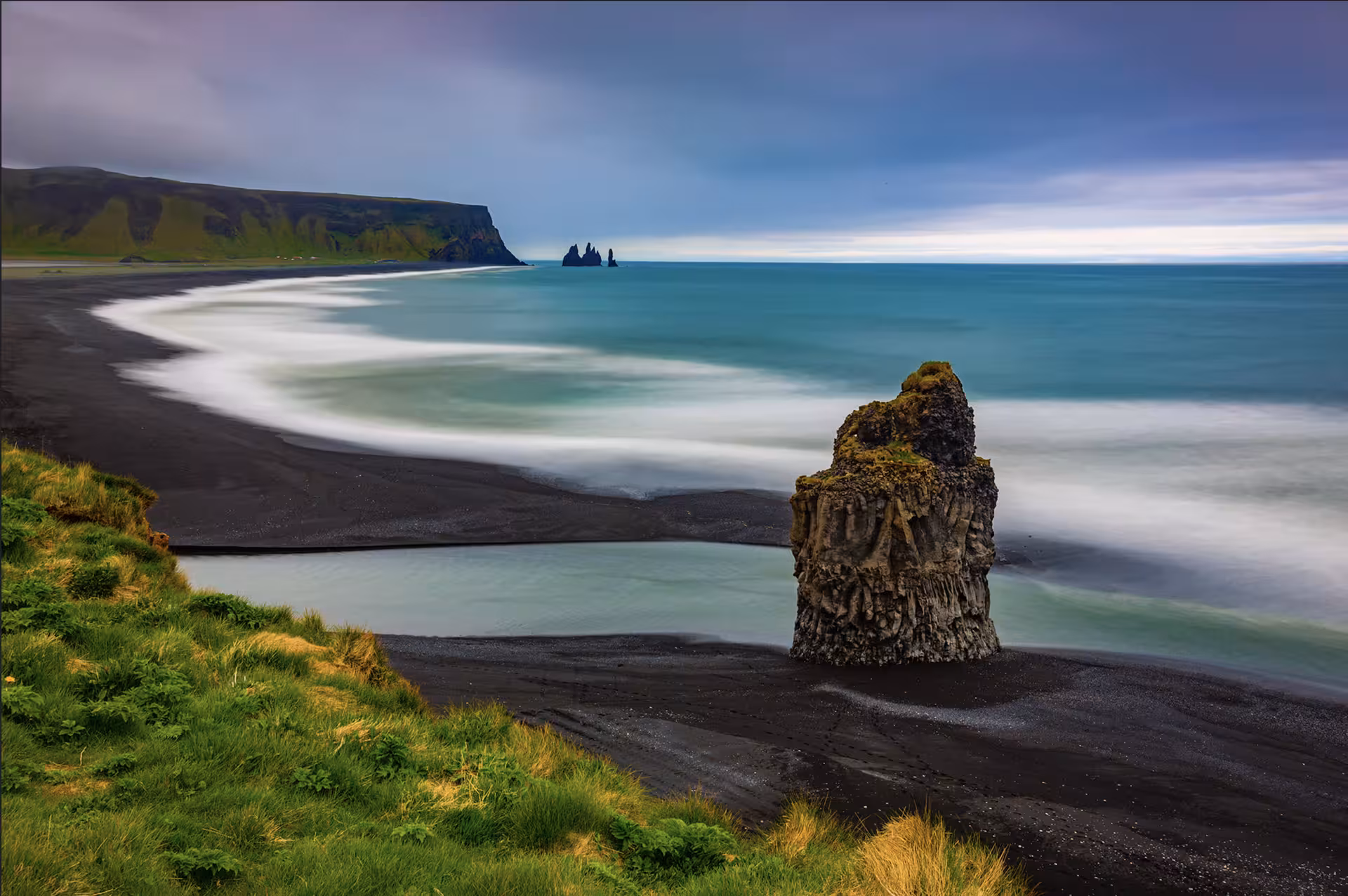 Black sand beach with volcanic rock stack and turquoise waves on Iceland's South Coast