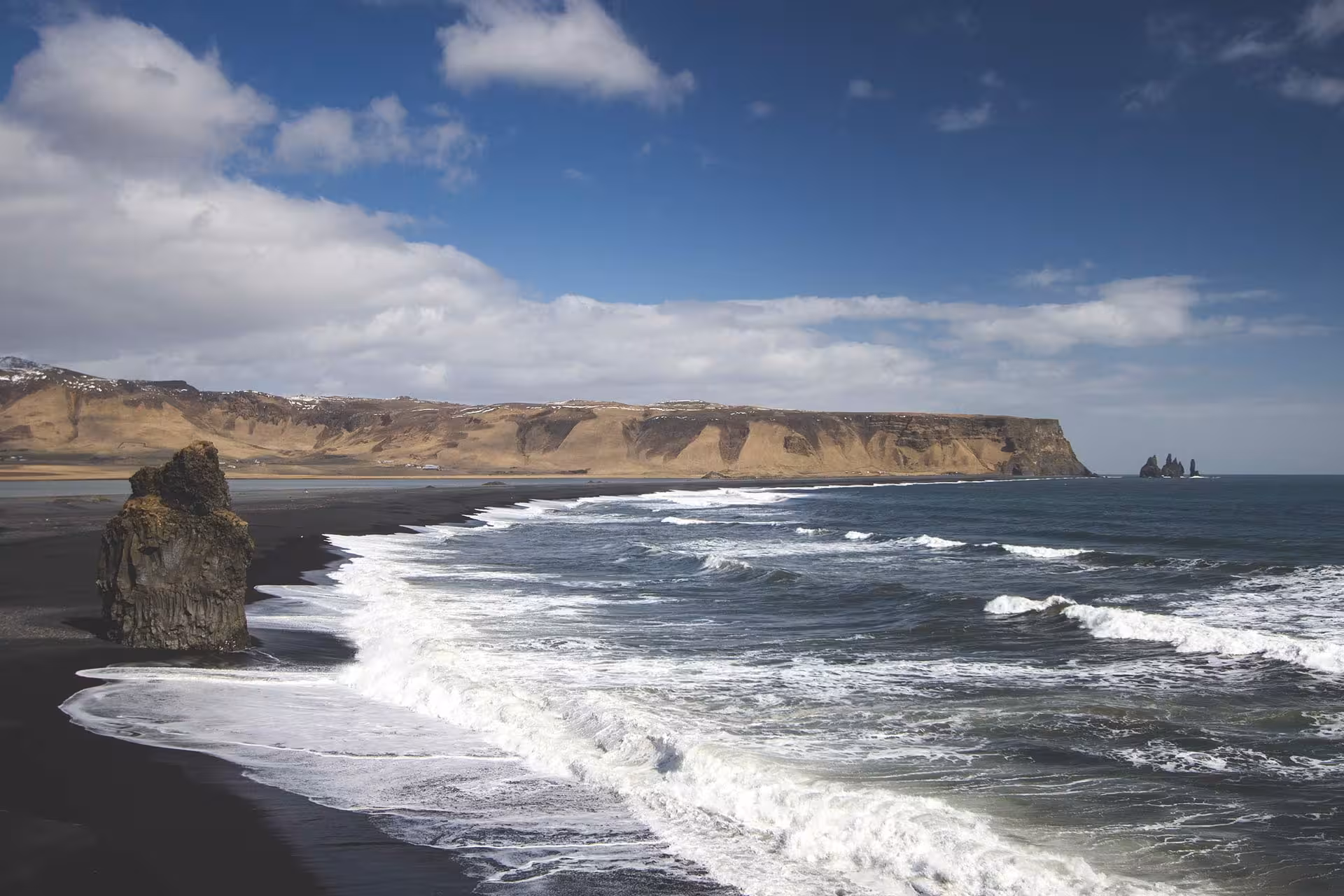 Black sand beach with crashing waves, sea stacks, and coastal cliffs on Iceland's South Coast