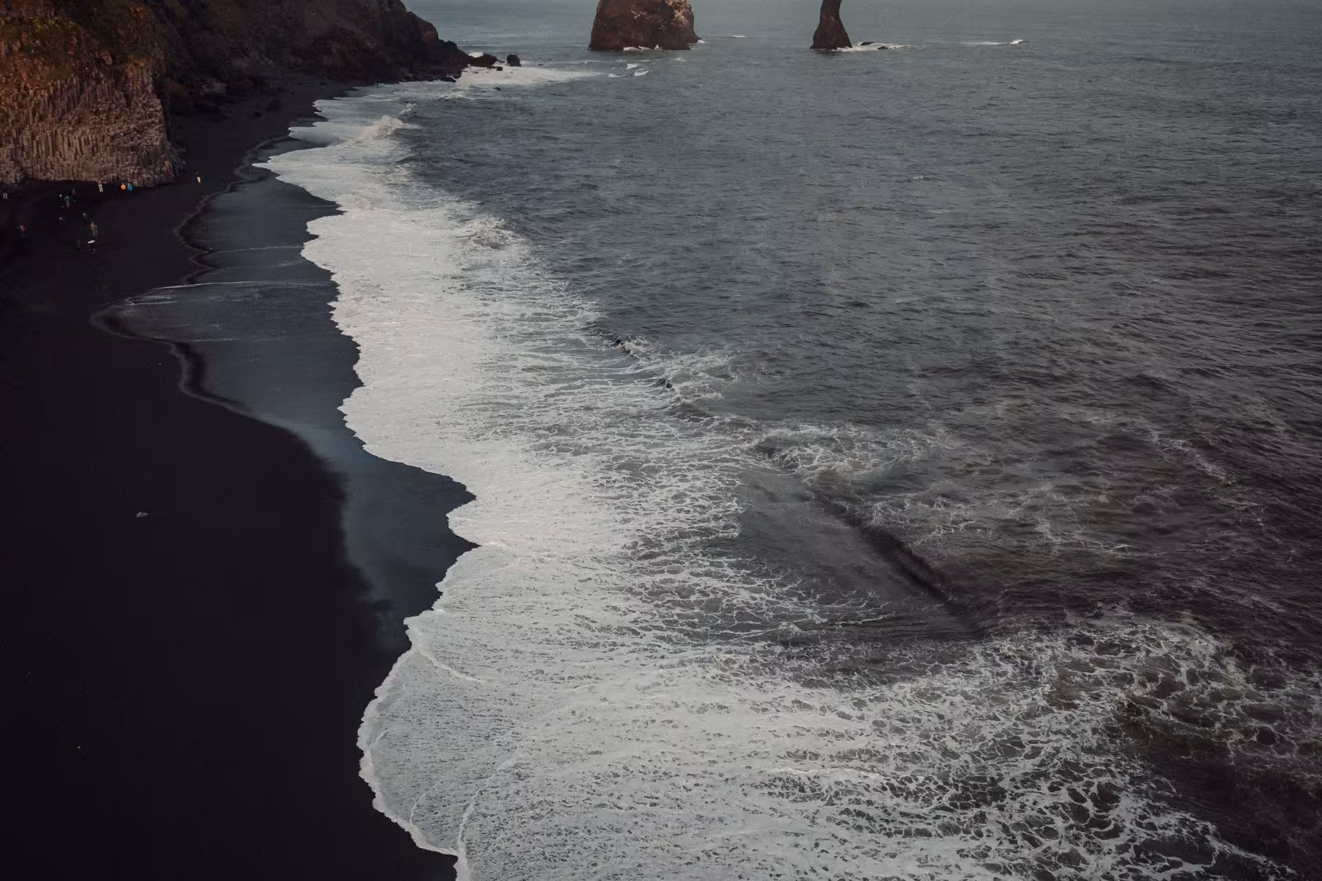 Aerial view of black sand beach with white ocean waves and volcanic rock stacks, Iceland south coast
