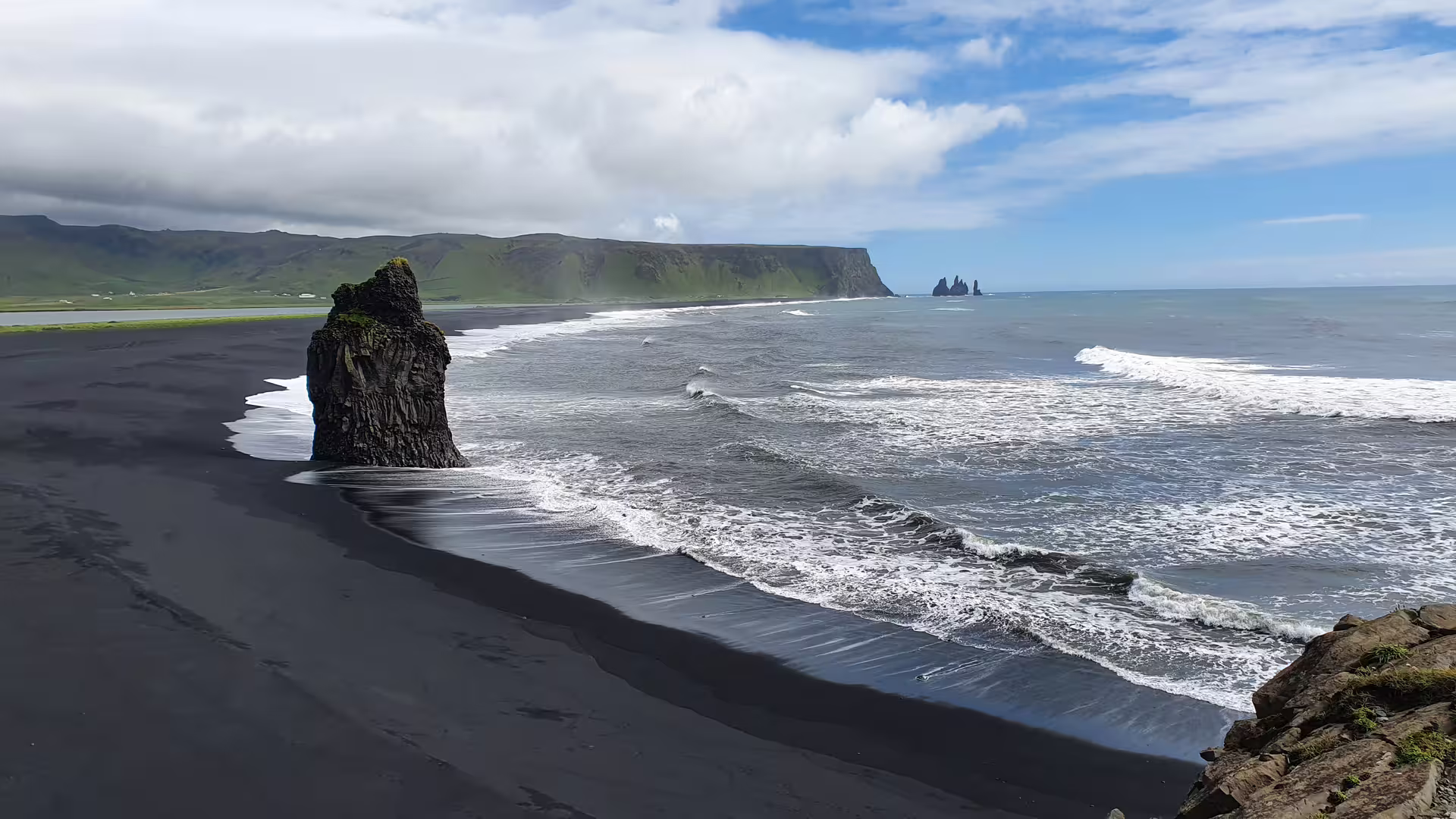 Black sand beach with volcanic rock stack and Reynisdrangar sea stacks along Iceland's south coast