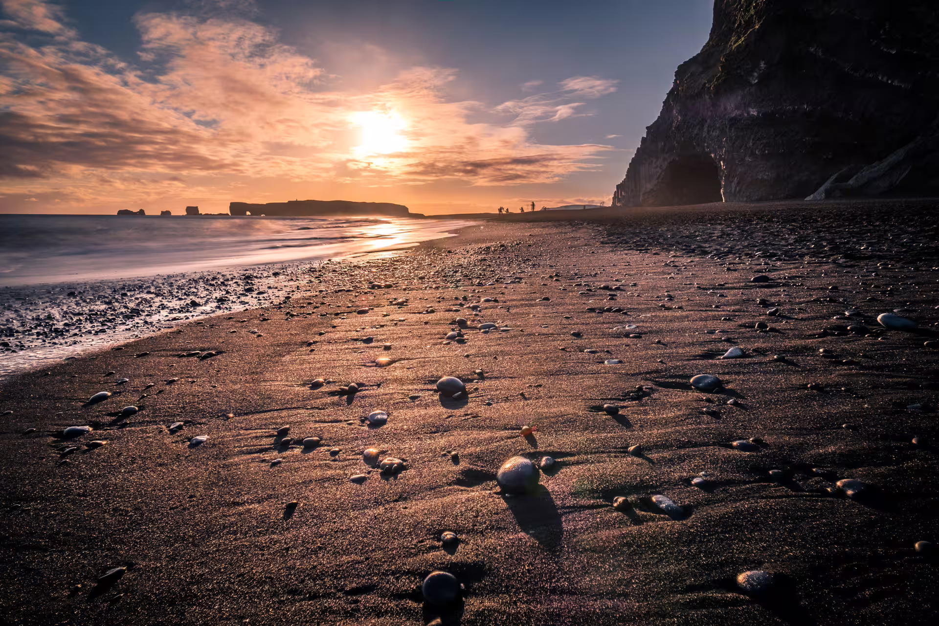 Black sand beach with pebbles at sunset near dramatic sea stacks and cliffs in Iceland