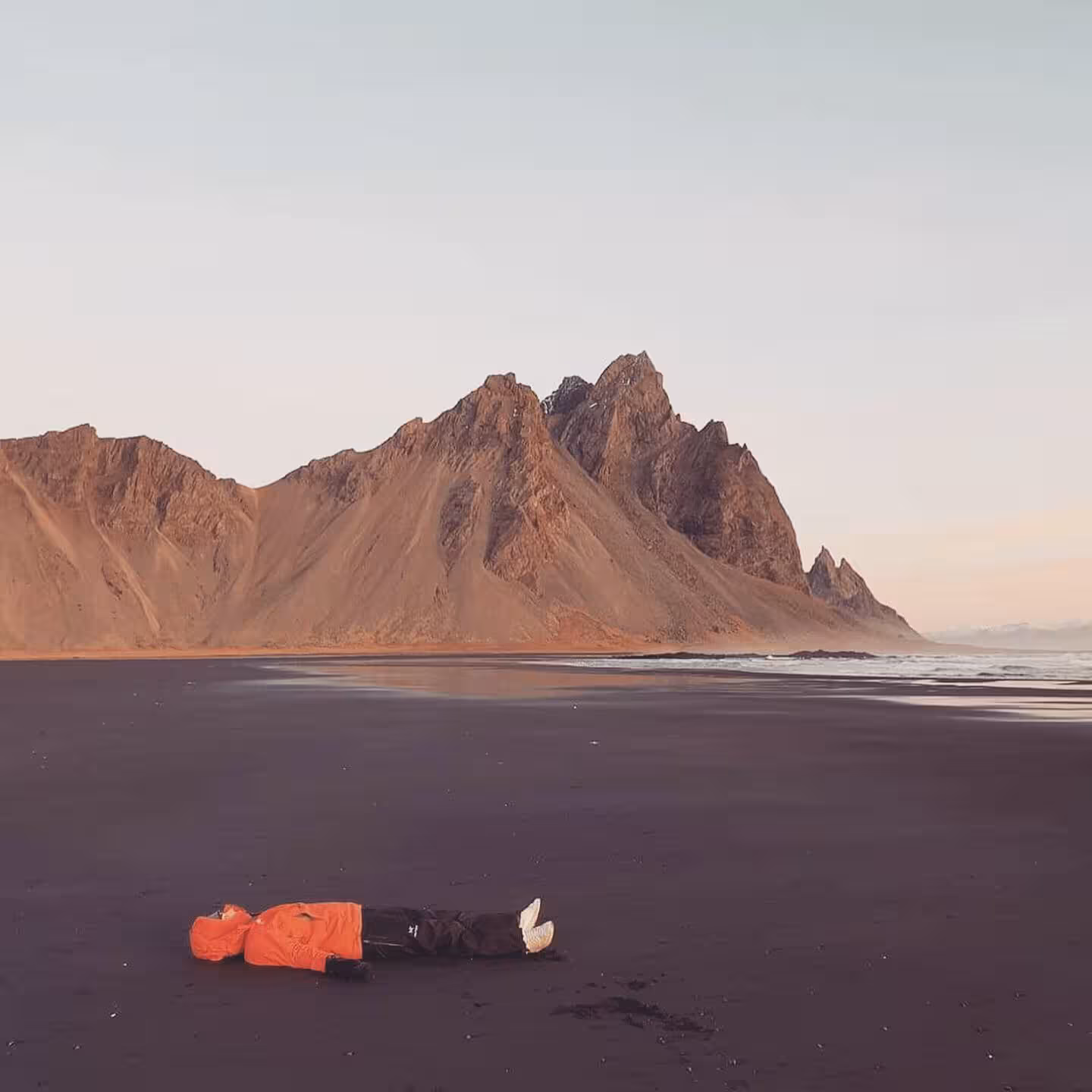 Person lying on black sand beach with dramatic Vestrahorn mountain backdrop in Southeast Iceland