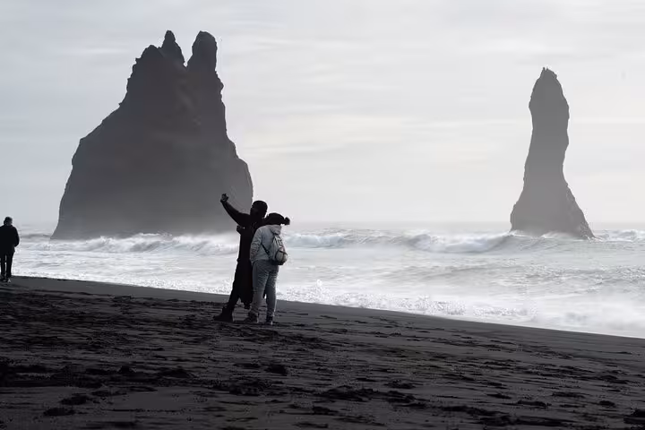 Tourists taking selfie on black sand beach at Reynisfjara with dramatic basalt sea stacks in Iceland
