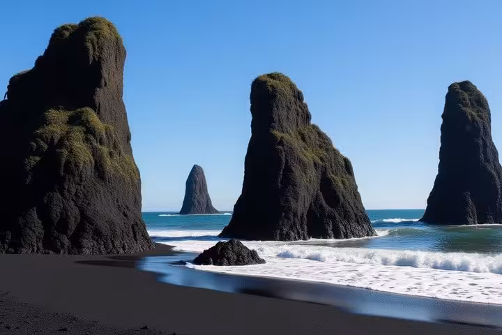 Black sand beach with tall moss-covered volcanic sea stacks rising from the ocean on Iceland's South Coast