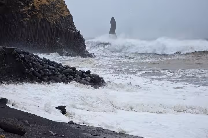 Powerful waves crashing on Reynisfjara black sand beach with basalt columns and sea stack in Iceland