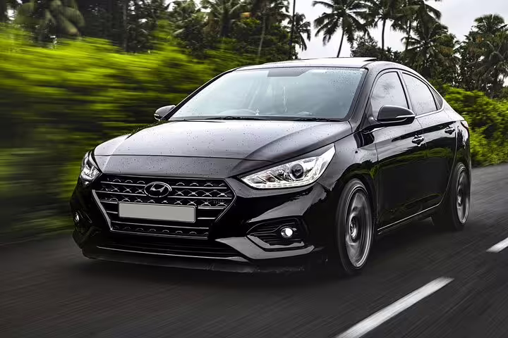 Black Hyundai sedan chauffeur transfer car driving on road with tropical trees in background
