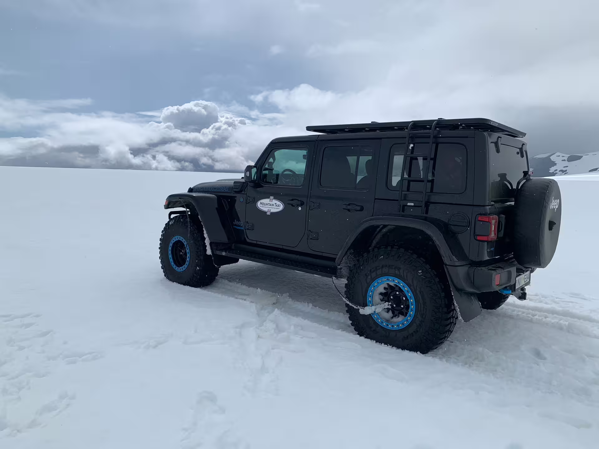 Black super jeep with blue beadlock wheels parked on a snow-covered glacier under cloudy skies