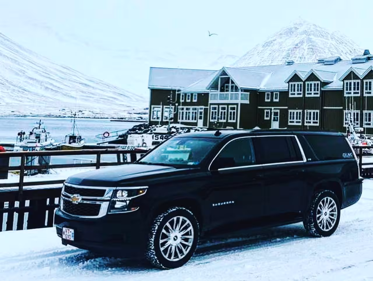 Black Chevrolet Suburban SUV parked in snowy Icelandic fjord town with snow-capped mountains